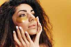 沉思的有吸引力的拉丁夫人黄金水凝胶补丁眼睛触摸软皮肤摆姿势孤立的黄色的背景化妆品产品自然美护肤品概念复制空间