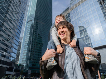 男孩坐在父亲的肩膀摩天大楼爸爸儿子玻璃墙建筑未来现代技术生活平衡家庭生活区