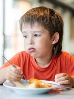 挑剔的孩子红色的t恤吃煎饼刀叉男孩有趣的表达式脸美味的糕点早餐