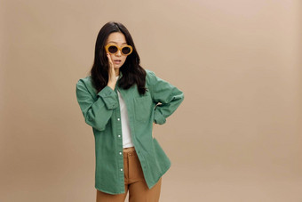 嘘兴奋震惊了朝鲜文年轻的女人卡其色绿色衬衫时尚的眼镜告诉流言蜚语摆姿势孤立的米色柔和的工作室背景很酷的时尚提供太阳镜概念