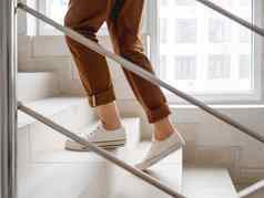 女人白色运动鞋卡其色裤子楼上公寓白色楼梯公寓建筑休闲装城市时尚物理练习
