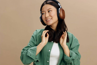 享受快乐可爱的亚洲学生年轻的女人卡其色绿色衬衫触摸耳机摆姿势孤立的米色柔和的工作室背景很酷的时尚提供音乐应用程序平台概念