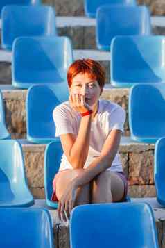 年轻的女人短红色的头发坐在放松塑料蓝色的座位废弃的开放空气观众夏天共鸣
