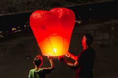 普吉岛泰国11月男人。男孩释放心形状的中国人飞行灯笼父亲儿子传统的节日阿来水灯