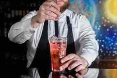 手专业酒保激起红色的糖浆含酒精的鸡尾酒酒吧勺子酒吧计数器过程准备含酒精的饮料