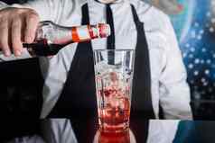 手专业酒保倒红色的糖浆玻璃冰多维数据集过程准备含酒精的鸡尾酒