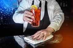 专业酒保持有手红色的含酒精的鸡尾酒冷冻喝玻璃装饰片切片柠檬湿巾酒吧计数器白色布服务