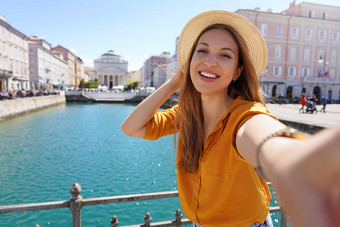 年轻的旅游女人使自拍照片站桥美丽的视图的里雅斯特城市意大利