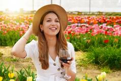 肖像漂亮的女人喝玻璃红色的酒用花装饰的背景一边快乐脸微笑