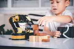 快乐亚洲孩子男孩远程控制玩机器人机手臂选择木块