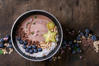 奶昔碗健康的早餐巧克力酸奶蓝莓格兰诺拉麦片椰子石灰杨桃黑暗木纹理背景画分支花前视图空间