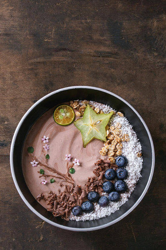 奶昔碗健康的早餐巧克力酸奶蓝莓格兰诺拉麦片椰子石灰杨桃黑暗木纹理背景画分支花前视图空间