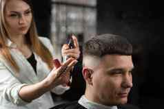 女人理发师使发型理发店限幅器理发师切割头发英俊的男人。