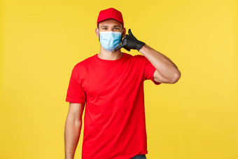 表达交付流感大流行科维德安全航运在线购物概念友好的年轻的邮件员工是快递红色的统一的医疗面具给调用订单