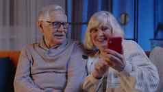 微笑高级夫妇祖母祖父使视频调用在线移动电话首页沙发