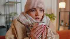 年轻的生病的女人穿他包装格子坐瑟瑟发抖冷沙发喝热茶