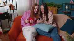 快乐的女孩朋友兄弟姐妹看照片智能手机沙发首页享受社会媒体
