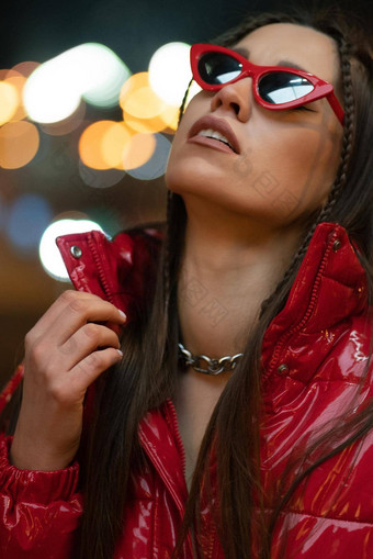 晚上生活时尚女孩太阳眼镜编织头发红色的光滑的外套站在户外晚上城市背景晚上生活概念晚上俱乐部生活概念