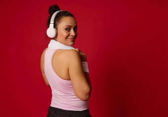 迷人的非洲运动女人运动服装无线耳机微笑肩膀相机放松锻炼孤立的红色的背景
