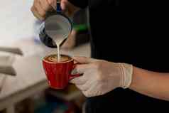 关闭咖啡师倒蒸牛奶咖啡杯使美丽的拿铁卡布奇诺咖啡艺术罗塞塔模式关闭咖啡师手倒温暖的牛奶红色的咖啡杯使拿铁艺术