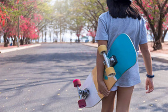 年轻的女孩手持有滑板冲浪滑冰公共路公园背景免费的放松滑板冲浪滑冰时尚的概念时尚肖像女手持有冲浪滑板