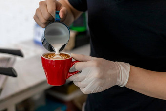 关闭咖啡师倒蒸牛奶咖啡杯使美丽的拿铁卡布奇诺咖啡艺术罗塞塔模式关闭咖啡师手倒温暖的牛奶红色的咖啡杯使拿铁艺术