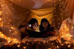 家庭概念老妹妹妹妹阅读书手电筒孩子们帐篷睡觉前快乐老妹妹读故事书妹妹床上表帐篷