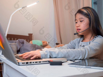 亚洲女孩耳机坐桌子上研究在线移动PC孩子穿耳机打字键盘笔记本<strong>学习</strong>互联网教训检疫女孩<strong>学生学习</strong>虚拟互联网在线类学校由于科维德流感大流行