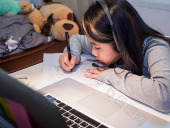 亚洲女孩耳机坐桌子上研究在线移动PC孩子穿耳机笔迹笔记本学习互联网教训检疫女孩学生学习虚拟互联网在线类学校由于科维德流感大流行