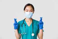 科维德冠状病毒疾病医疗保健工人概念特写镜头充满希望的亚洲女医生医生医疗面具橡胶手套使交叉手指好运气