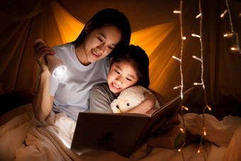 家庭概念妈妈。孩子女儿阅读书手电筒孩子们帐篷睡觉前快乐妈妈。读故事书女儿床上表帐篷