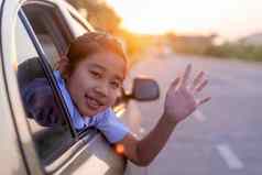 学校女孩拉伸手车窗口笑微笑亚洲女孩微笑挥舞着手车孩子们放松街视图车家庭车概念