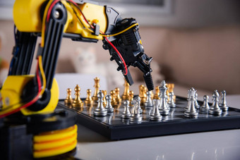 特写镜头黄色的机器人手臂玩移动国际象棋棋盘图片