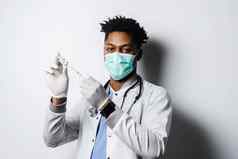 非洲医生冠状病毒科维德疫苗注射器黑色的男人。医疗面具使疫苗接种白色背景