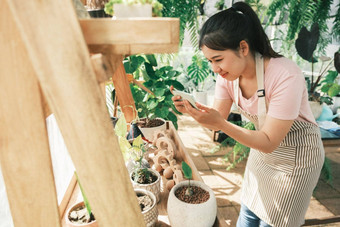 微笑年轻的女人采取智能<strong>手机图</strong>片植物小商店