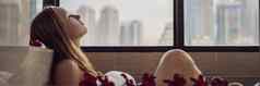 年轻的女人坐在浴泡沫鸡蛋花花背景全景窗口俯瞰摩天大楼大晚上城市横幅长格式