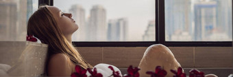 年轻的女人坐在浴泡沫鸡蛋<strong>花花</strong>背景全景窗口俯瞰摩天大楼大晚上城市横幅长格式