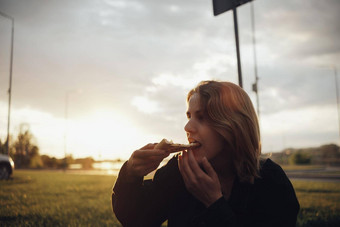 金发女郎女孩吃披萨坐着日落