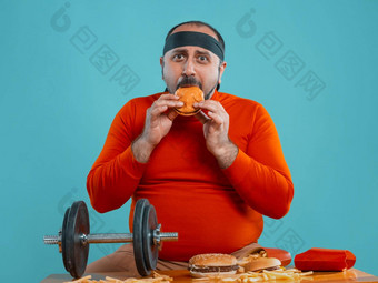 中年男人。胡子穿着红色的<strong>高领</strong>毛衣头巾摆姿势汉堡法国薯条蓝色的背景特写镜头快食物