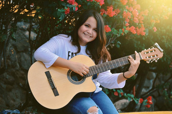 女孩坐着玩吉他在户外肖像微笑女孩玩吉他生活方式女孩玩吉他在户外