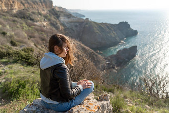 女人旅游享受日落海山景观坐在在户外岩石海穿牛仔裤蓝色的连帽衫黑色的皮革夹克<strong>健康</strong>的生活方式<strong>和谐</strong>冥想