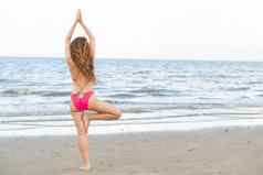 年轻的女人实践瑜伽海滩夏天