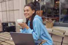 美丽的年轻的混血快乐的女人穿刺持有咖啡微笑咖啡馆阳台