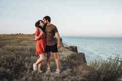 快乐的年轻的夫妇站背景海快乐男人。拥抱卷曲的女人红色的衣服日落