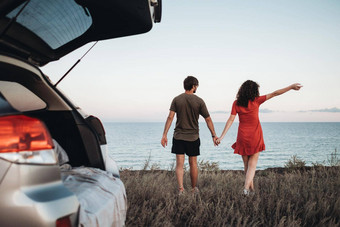 年轻的夫妇持有手走背景海男人。女人享受路旅行车