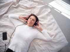 女人放松床上眼睛关闭听音乐移动