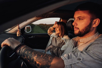 纹身高加索人男人。年轻的女人坐着车日落夫妇享受路旅行周末