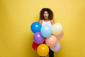庆祝活动概念关闭肖像快乐年轻的美丽的非洲女人白色t恤微笑色彩斑斓的聚会，派对气球黄色的柔和的工作室背景