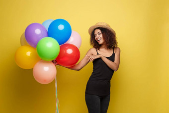 庆祝活动概念关闭肖像快乐年轻的美丽的非洲女人黑色的t恤微笑色彩斑斓的聚会，派对气球黄色的柔和的工作室背景