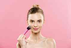 美概念特写镜头美丽的高加索人女人应用化妆化妆品粉刷完美的皮肤孤立的粉红色的背景复制空间